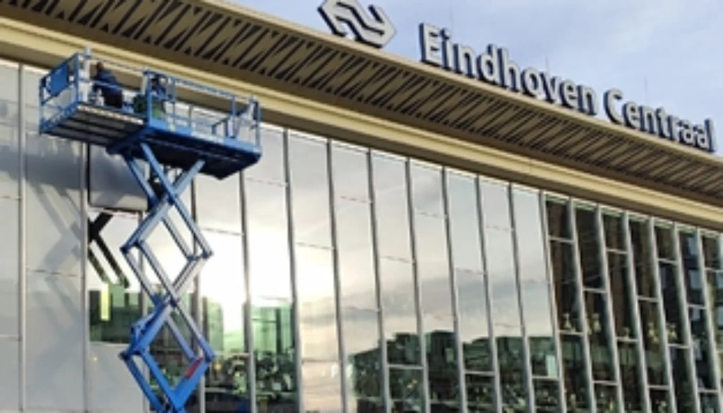 Aanbrengen van zonwerende raamfolie op de glasgevel van station Eindhoven Centraal met hoogwerker.