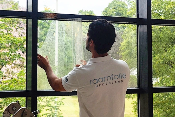 Monteur brengt veiligheidsfolie aan op raam van een woning voor extra bescherming